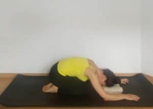 Image of a women in child's pose with a pillow under her forehead. This pose is perfect to lower cortisol levels.