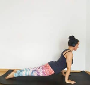 Image of a woman in upward facing dog pose, wearing headphones to spice up her yoga practice at home with some music