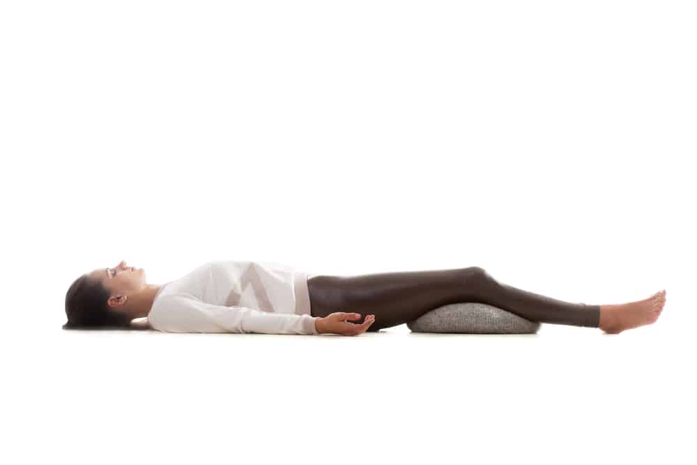 Image of a woman in shavasana pose, a pillow under her knees for extra padding